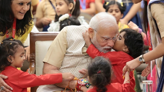 Prime Minister Narendra Modi is surrounded by school children as they tie rakhi on his wrist during Raksha Bandhan celebrations at his residence. (X/BJP)